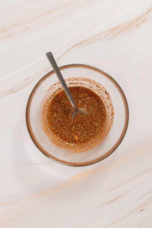 Fresh homemade vinaigrette with herbs in a glass bowl on a wooden surface.