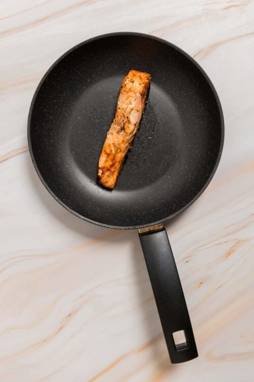 Pan-fried salmon fillet cooking in a black non-stick skillet.
