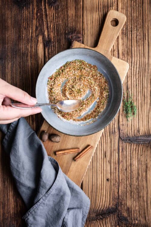 Ground spice mixture in a gray skillet with wooden handle on rustic wood surface.