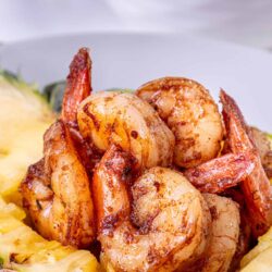 Juicy shrimp and lobster served in a hollowed pineapple half, garnished with herbs, for tropical seafood dish.