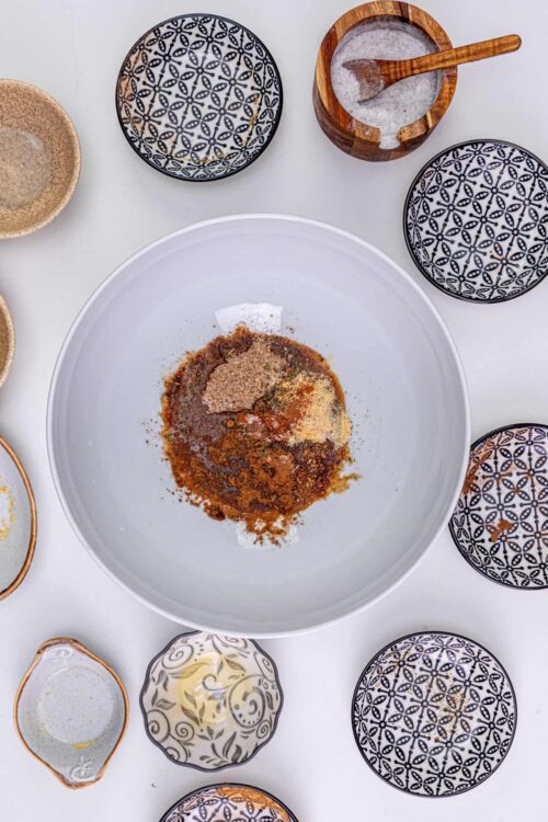 Ground spices and seasonings in a white mixing bowl with various patterned bowls around it.