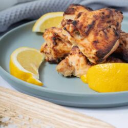 Juicy grilled chicken thighs with lemon wedges on a light blue plate.