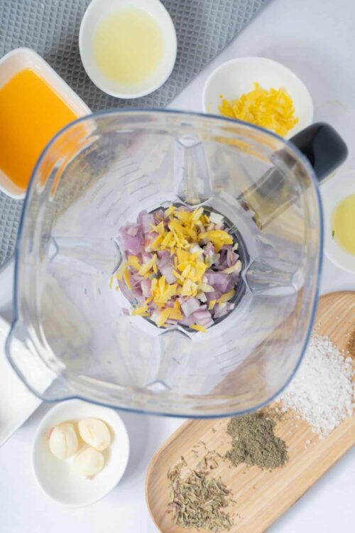 Chopped onions and shredded cheese in a blender, surrounded by spices and liquids for cooking.