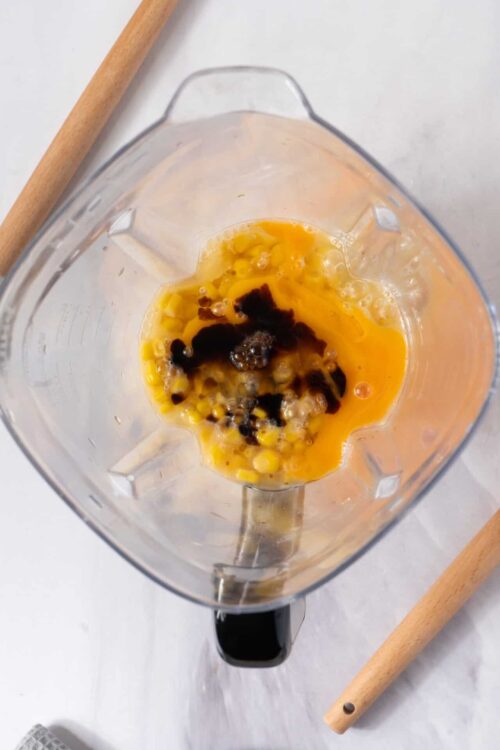 Blender with eggs, vanilla, and dark liquid for baking preparation, ingredient for desserts and baked goods.
