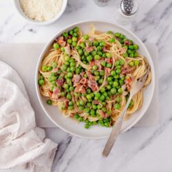 Creamy pea and bacon spaghetti dish served on a white plate.