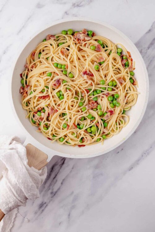 Creamy pasta with peas and bacon in a white bowl.