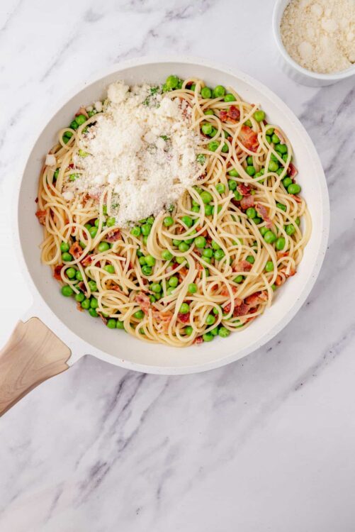 Creamy spaghetti with peas and bacon in a white skillet on marble surface.