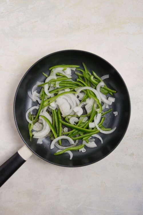 Sautéed onions and green peppers in a black skillet, ready for cooking or recipe preparation.