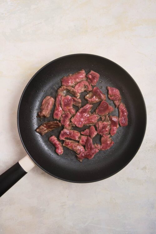 Sliced beef cooking in a non-stick skillet.
