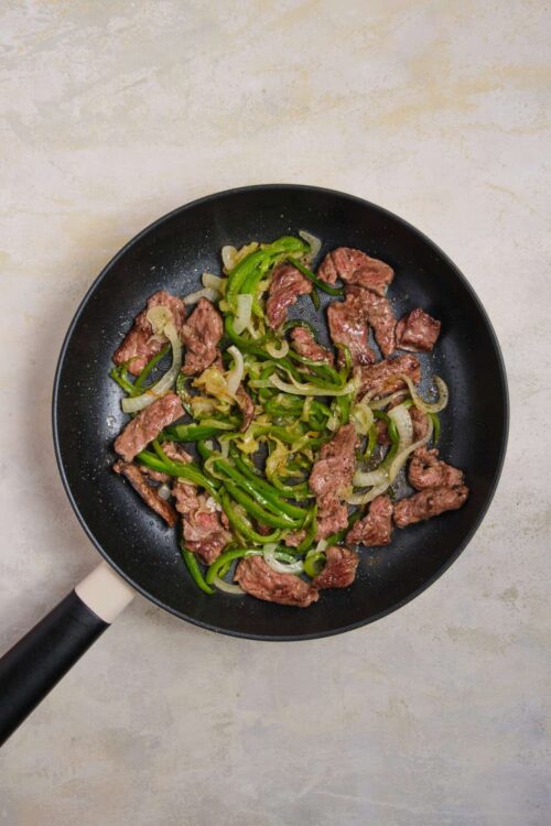 Sautéed beef and green bell peppers in a black skillet.
