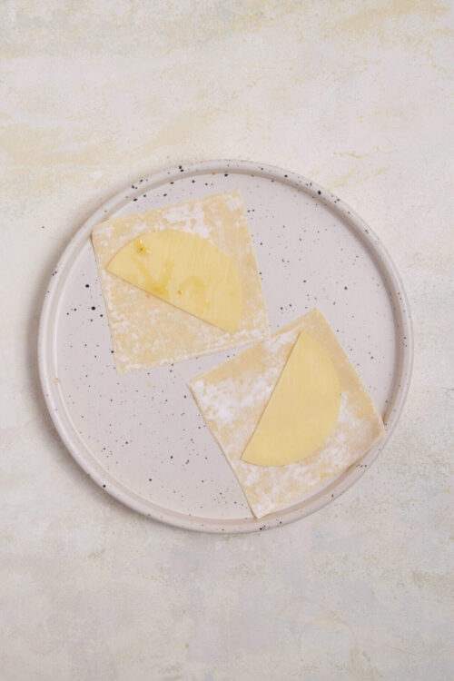 Buttery pastry with cheese slices on a white speckled plate.