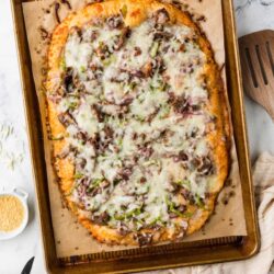Golden baked onion and mushroom flatbread with melted cheese on baking sheet.