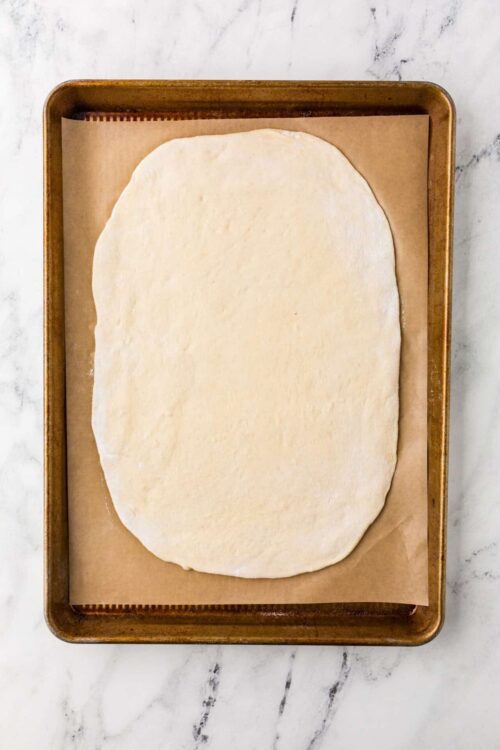 Soft pizza dough on baking sheet ready for baking, on white marble background.