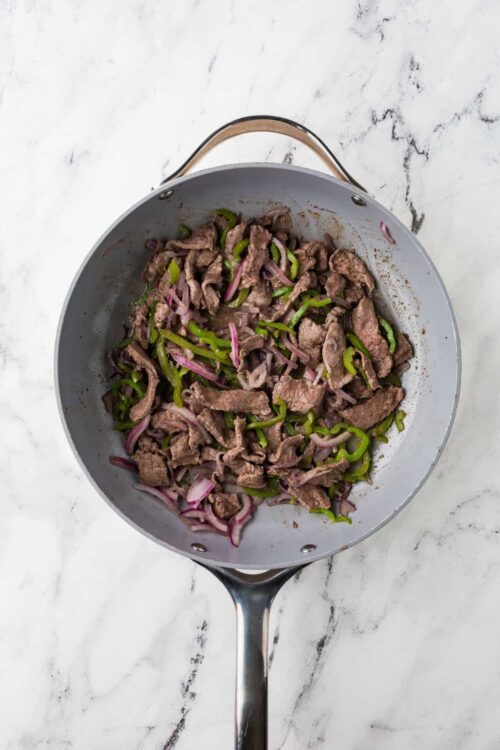 Sautéed beef with green peppers and red onions in a stainless steel skillet.