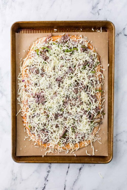 Cheesy pizza with shredded cheese, green peppers, onions, and ground beef ready for baking.