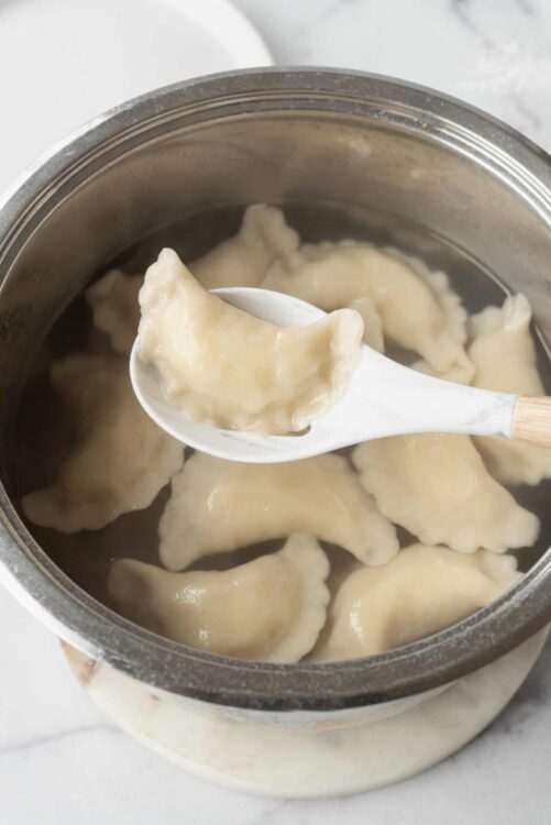 Pork dumplings in a steam pot with a wooden handled spoon.