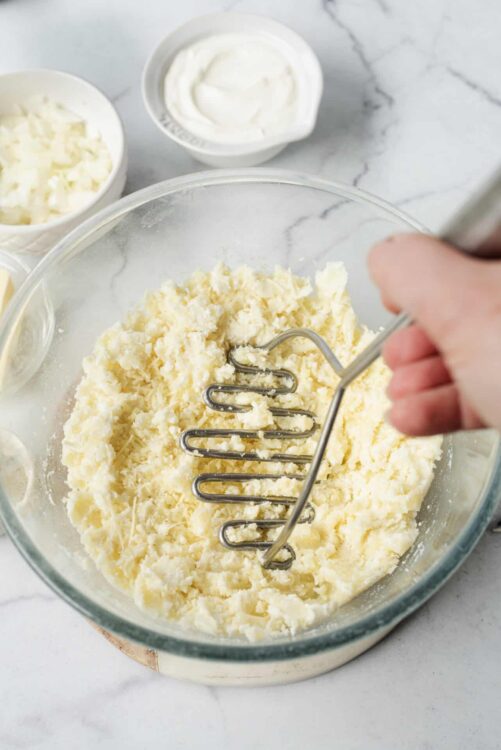 Creamy mashed potatoes being mixed with a hand mixer in a glass bowl for baking recipes.