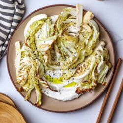 Roasted lemon garlic cabbage steaks with olive oil and black sesame seeds on a brown plate.