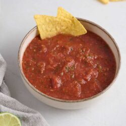Creamy homemade salsa in a rustic bowl with tortilla chips, lime, and cilantro on a white surface.