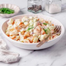 Creamy shrimp potato salad in a white bowl on marble surface.