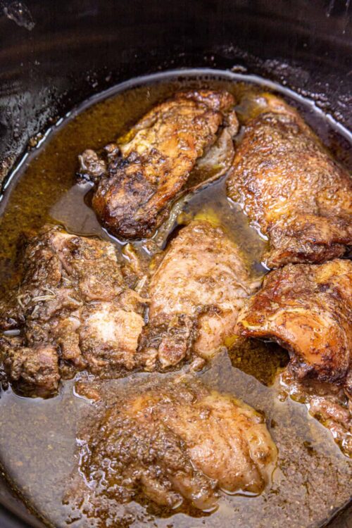Succulent slow-cooked chicken thighs in flavorful gravy within a cast iron skillet.