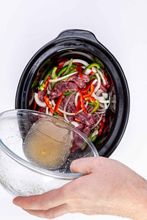 Sliced beef with colorful bell peppers and onions in a slow cooker for beef stir-fry or Asian-inspired recipes.