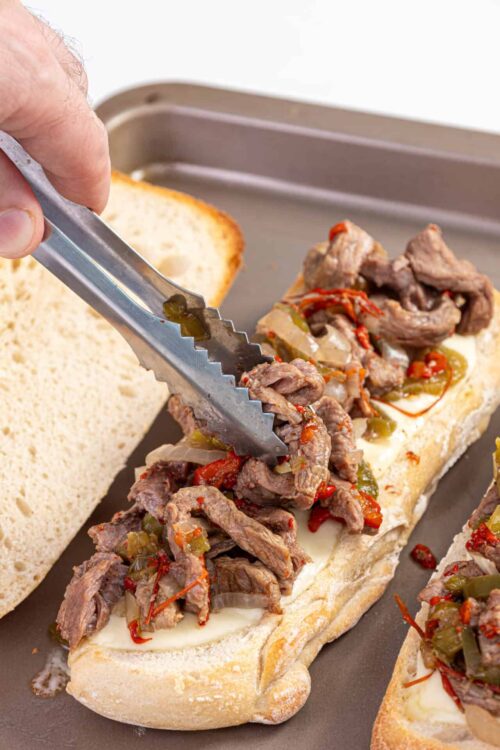 Slow cooker beef sandwich on hoagie roll with melted cheese and sautéed peppers.