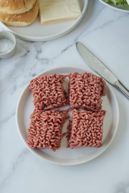 Raw ground beef patties on a white plate for burger recipes.