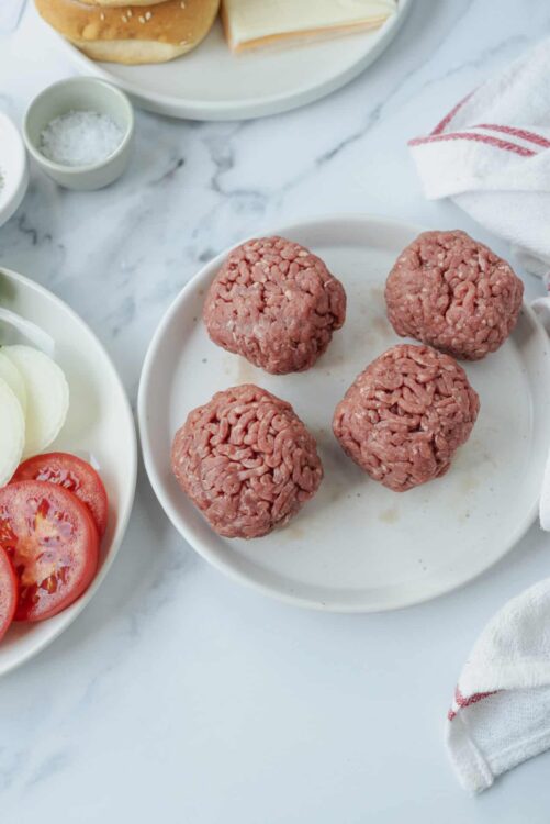 Seasoned ground beef meatballs on white plate for baking or cooking.