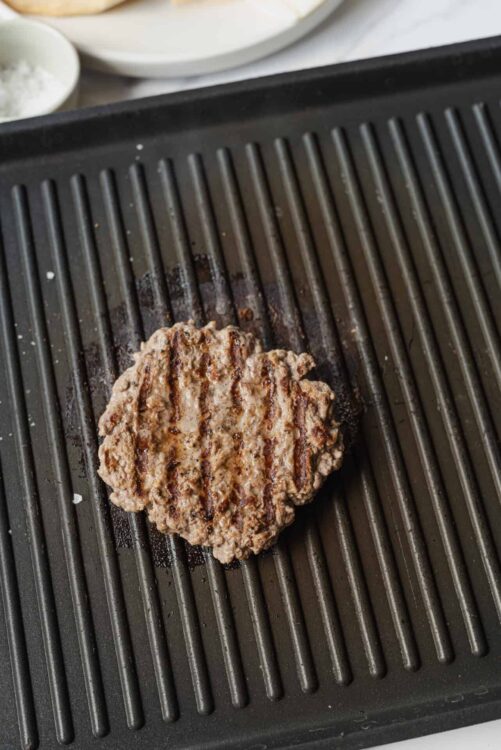 Grilled burger patty on a black griddle, ready for assembling in a delicious homemade burger.