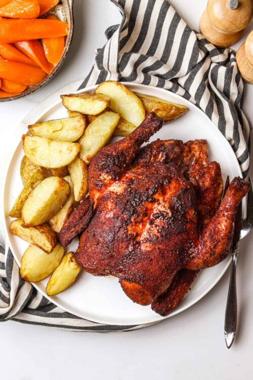 Crispy roasted chicken with seasoned potatoes and carrots on a white plate.