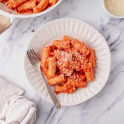 Creamy tomato basil baked pasta with grated Parmesan cheese on white plate.