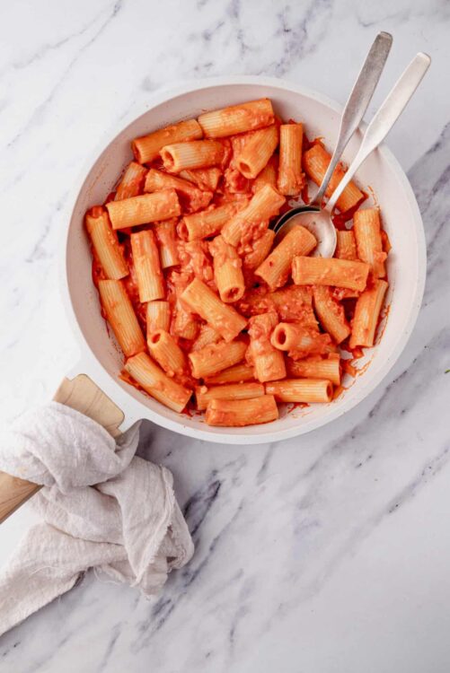 Pasta with tomato sauce in a white bowl on marble surface, ready to serve.