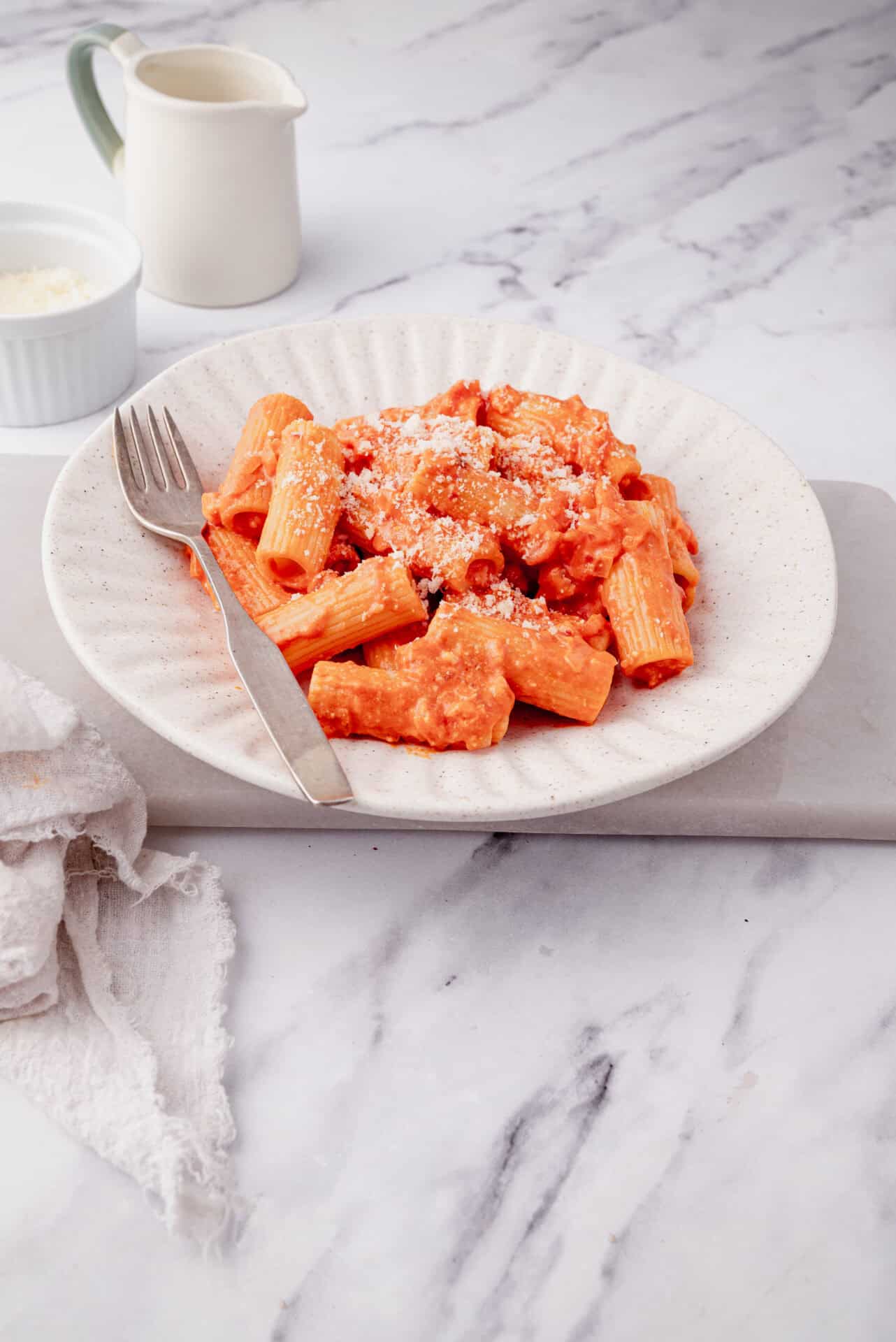 Creamy tomato pasta with grated Parmesan cheese on a textured white plate.