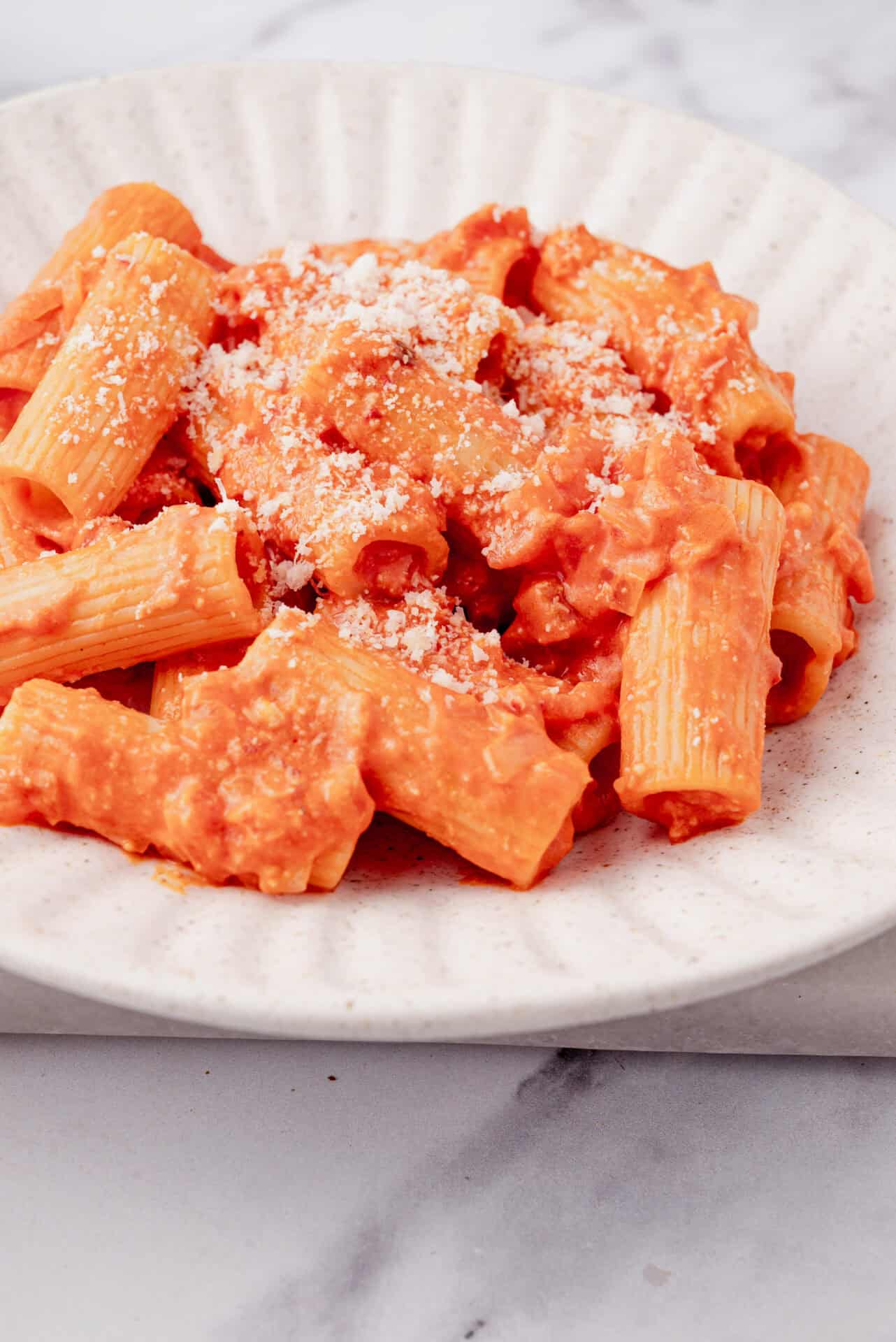 Creamy tomato basil pasta with parmesan cheese on a white plate.
