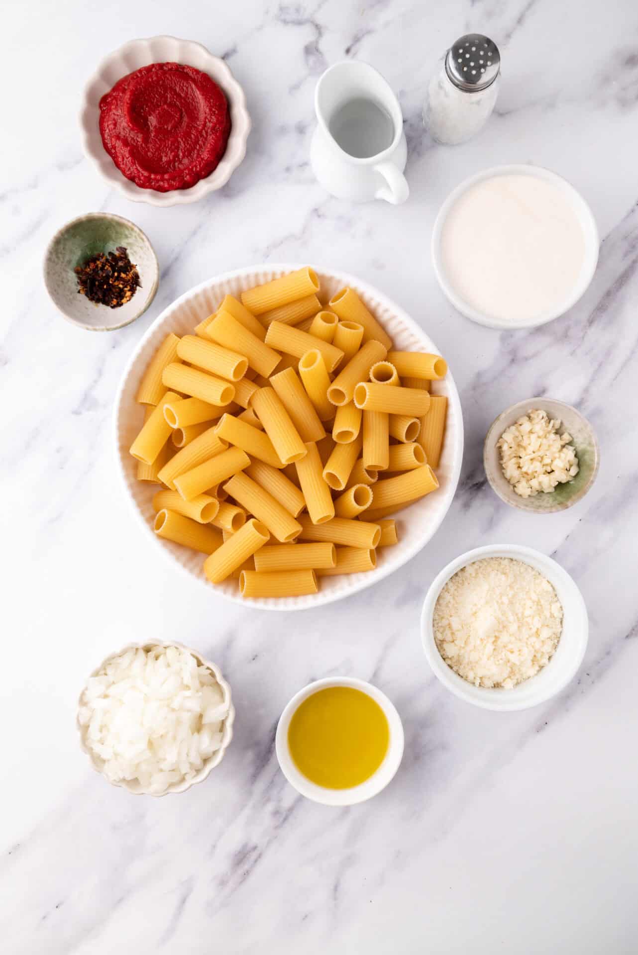 Cooked pasta with cheese and tomato sauce ingredients on a marble surface.