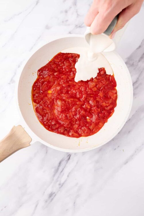 Rich tomato sauce simmering in a white skillet with a wooden handle.