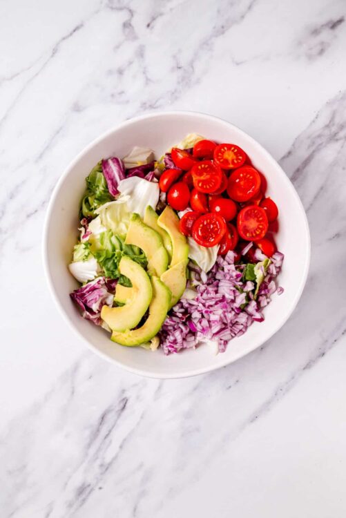 Fresh cherry tomato, avocado, lettuce, red onion, and radicchio in a bowl - healthy salad ingredients.