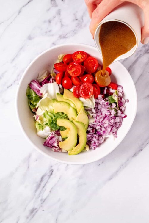 Fresh vegetable salad with cherry tomatoes, avocado, and red onion drizzled with dressing.