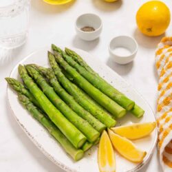 Fresh roasted asparagus with lemon wedges on a white platter, ideal for healthy side dishes or spring vegetables.