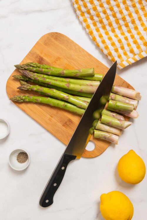 Fresh asparagus spears on a wooden cutting board with a chef's knife for preparation.