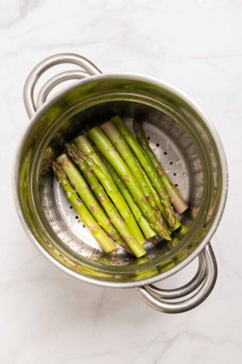 Fresh steamed asparagus in a stainless steel steamer basket.