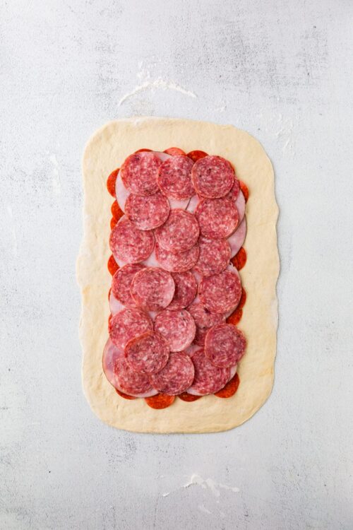 Slices of pepperoni and ham on pizza dough before baking, ready to make homemade pizza.