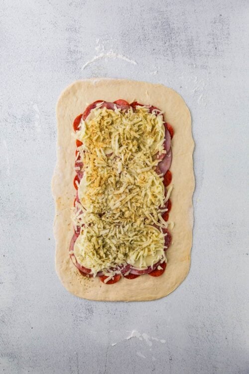 Shredded cheese and sliced pepperoni pizza filling on pizza dough before baking.