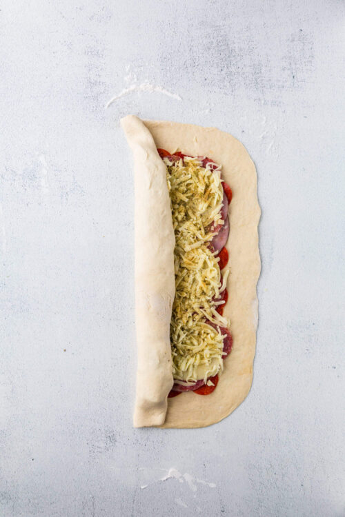 Fresh uncooked pizza dough with cheese, pepperoni, and vegetables ready to bake.