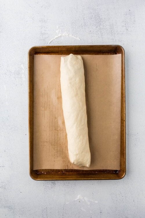 Unbaked bread dough loaf on parchment paper in a baking tray.