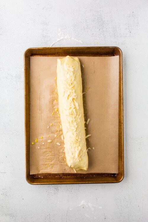 Cream cheese and shredded cheese rolled pastry on baking sheet for cheesy appetizer or baked good.
