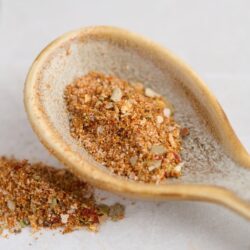 Cajun seasoning mix in a beige spoon on a white surface.