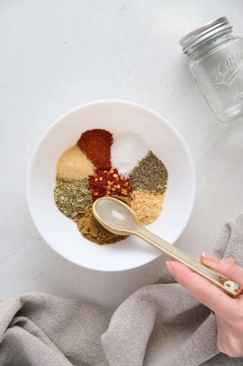 Mixed spices for baking in a white bowl with a gold spoon on a light background.