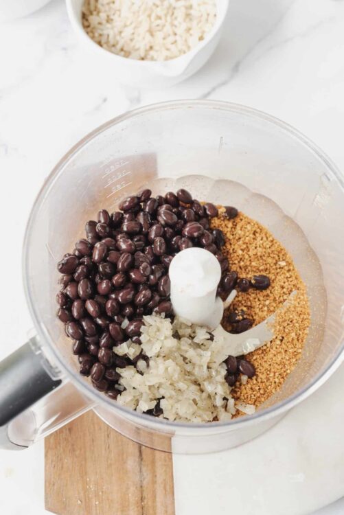 Creamy black beans, chopped onions, and toasted breadcrumbs in a food processor bowl for homemade bean dip.